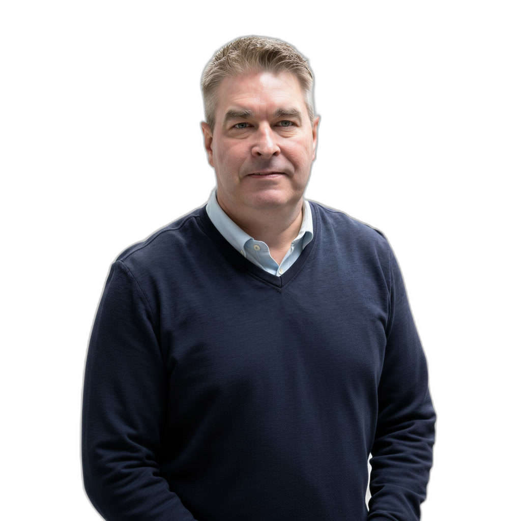 A middle-aged man with short, light brown hair wearing a navy sweater over a light blue collared shirt stands against a plain white background.